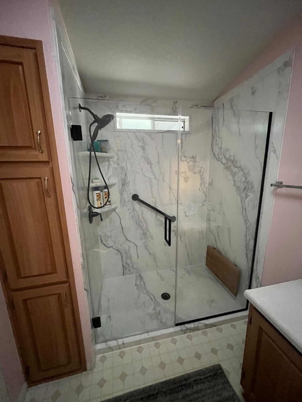 Marble-look shower with a matte-black grab bar and fold-down teak bench